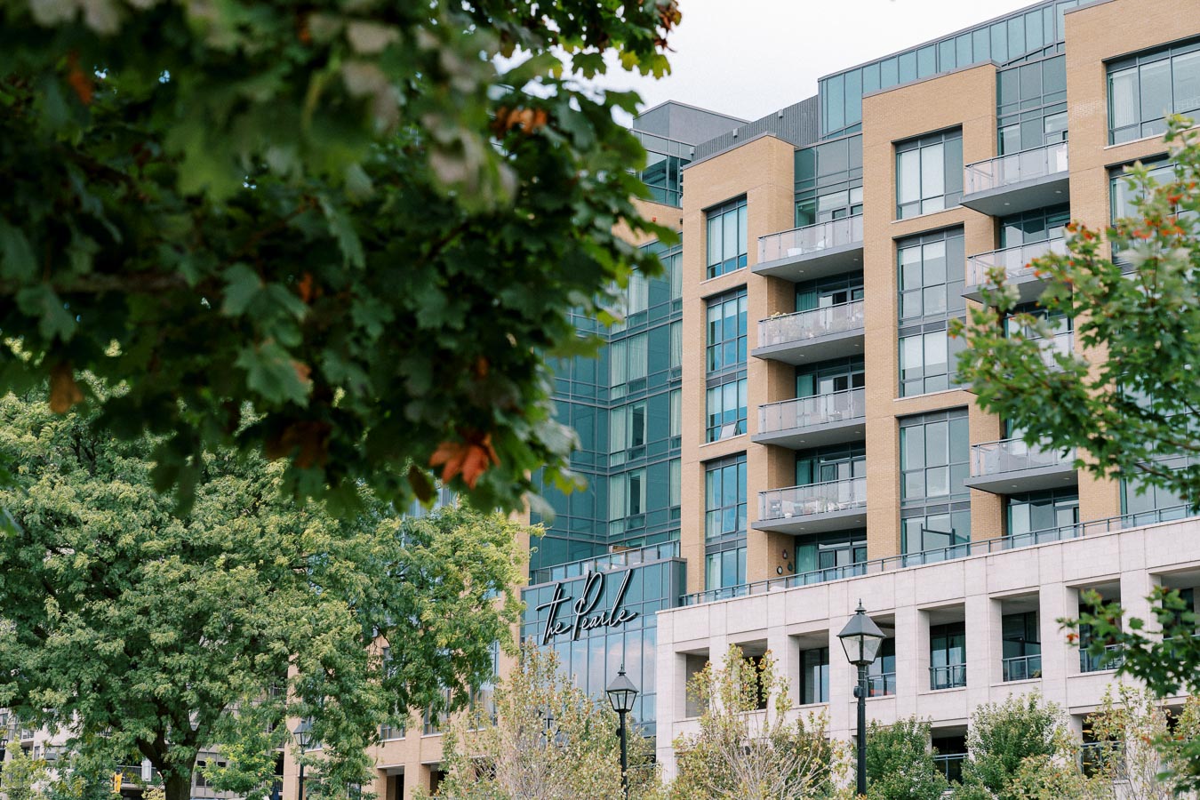 Modern multi-story building with glass balconies surrounded by lush green trees