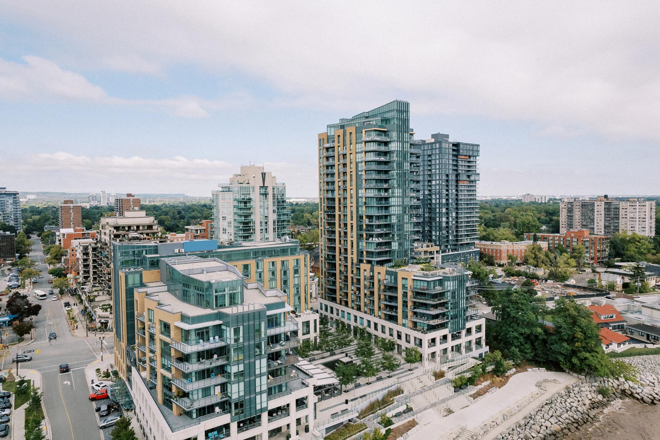 Aerial view of modern waterfront condominiums surrounded by greenery and a cityscape, showcasing urban living and architecture.