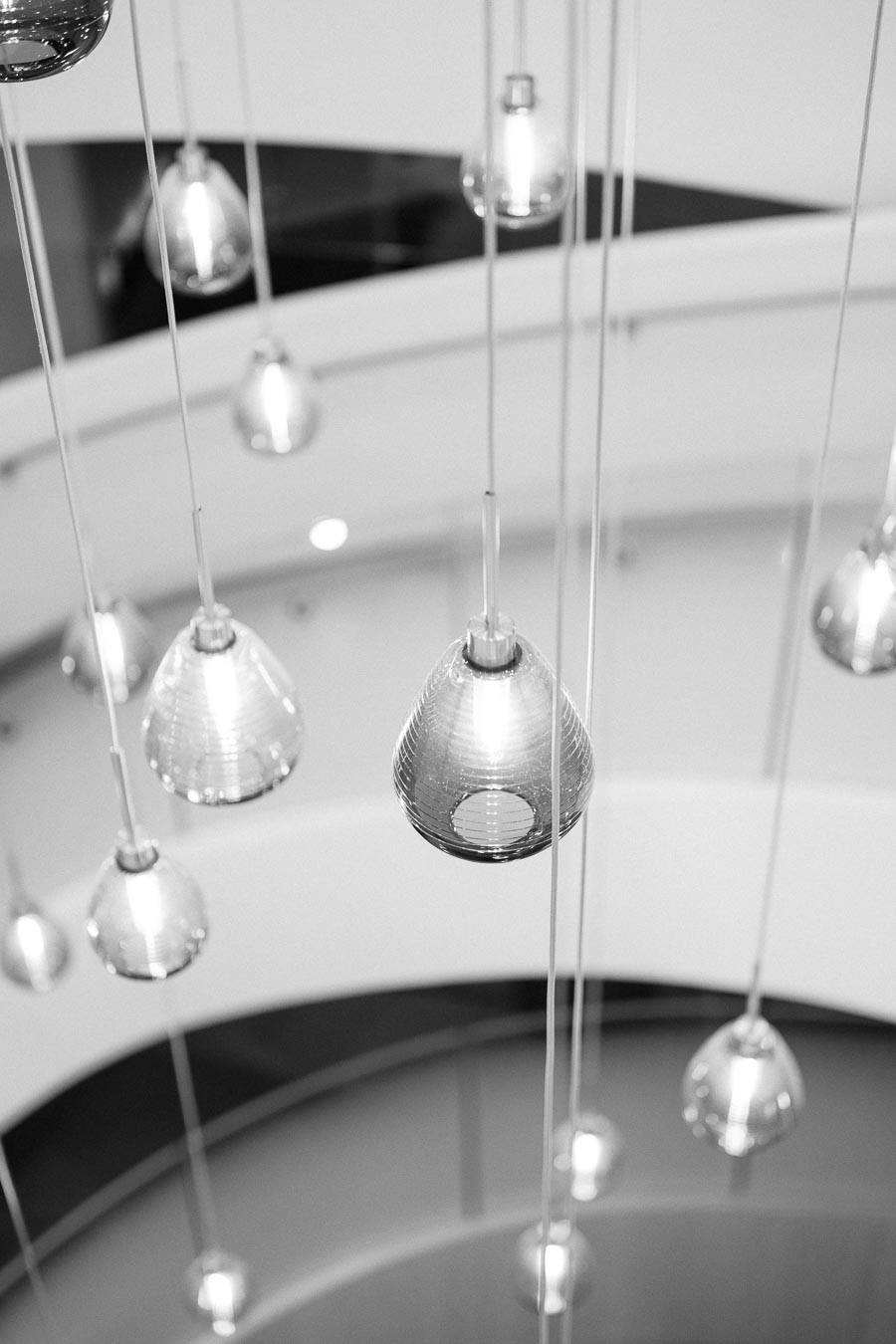 Black and white photo of modern pendant lights hanging in a spiral formation, creating an elegant and contemporary lighting design in an architectural space.