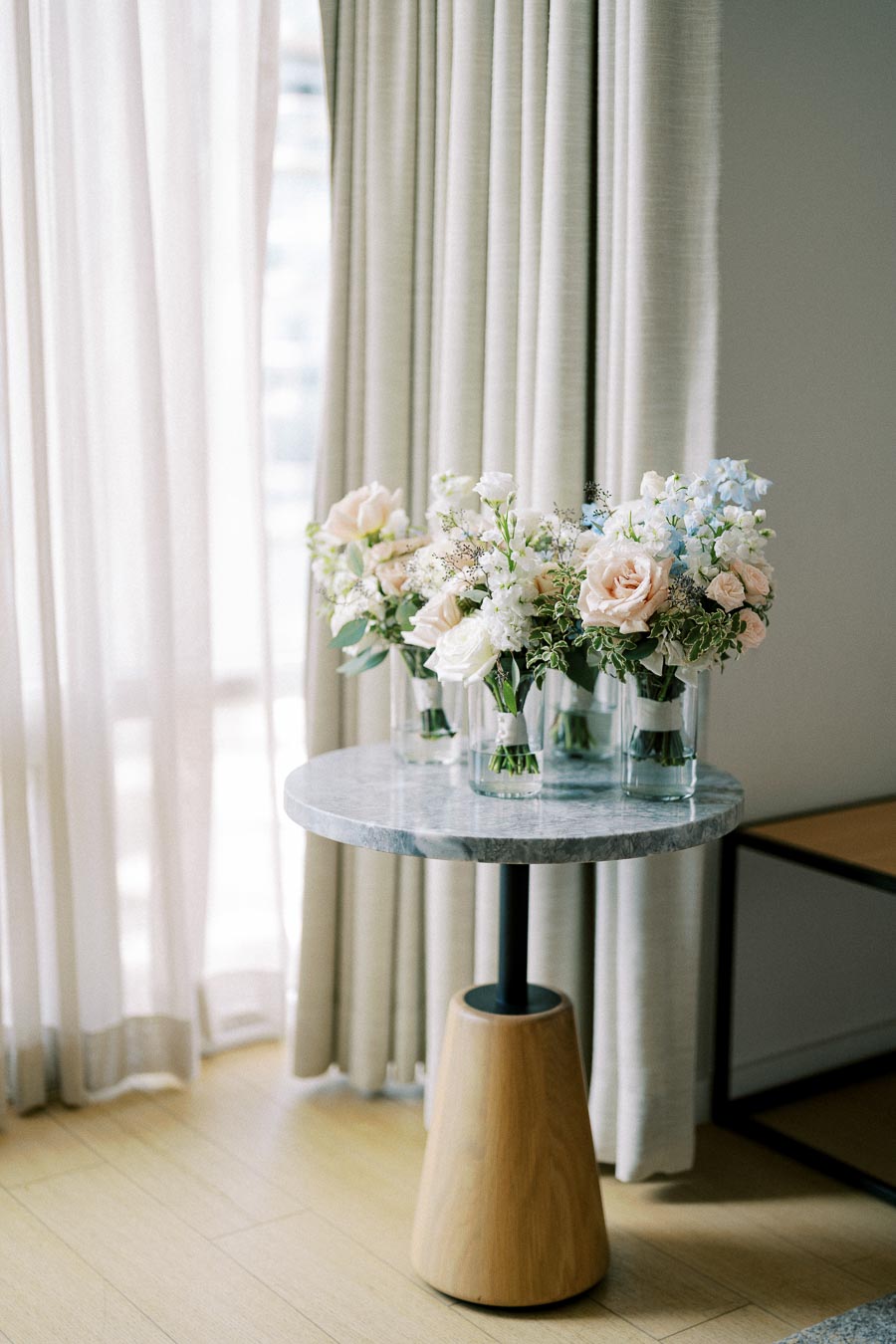 Elegant marble-top side table with vases of pastel pink and white roses in a softly lit room with sheer curtains.