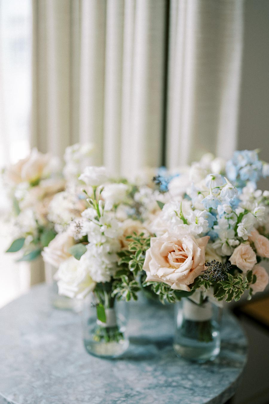 Elegant pastel flower arrangement with roses and delphiniums in glass vases on a marble table, creating a sophisticated and serene atmosphere.
