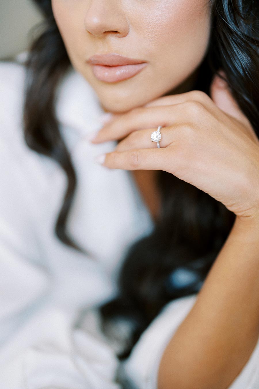 Close-up of a woman wearing a sparkling diamond engagement ring on her finger, with elegantly manicured nails and smooth, glossy lips, capturing the essence of luxury and elegance.