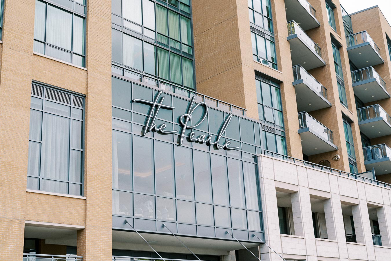 Modern hotel building facade with glass balconies, featuring 'The Pearle' signage, representing contemporary architecture and urban design.