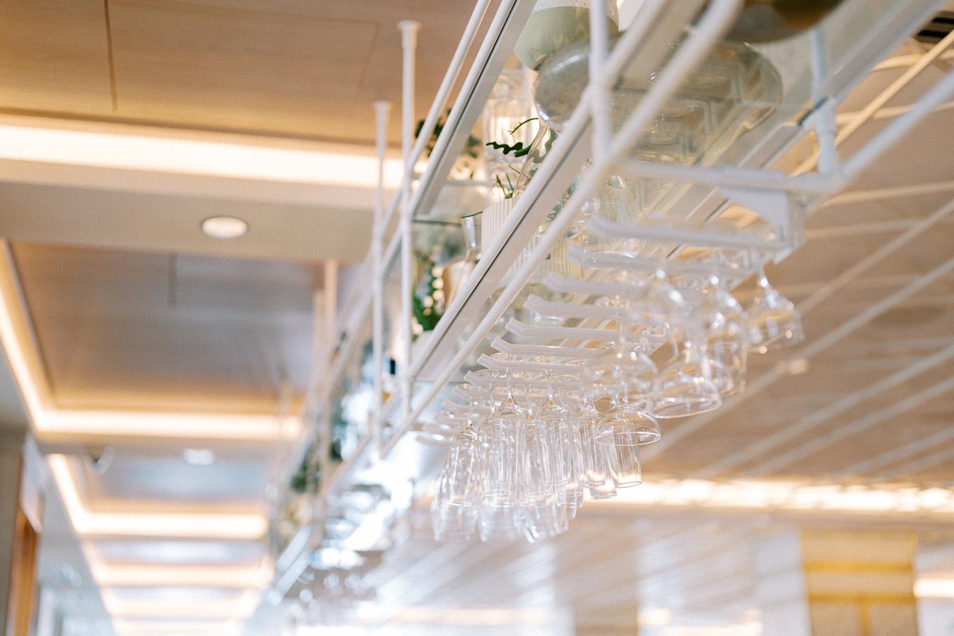 Alt text: Close-up of an elegant bar rack with hanging wine glasses in a modern, well-lit restaurant interior.