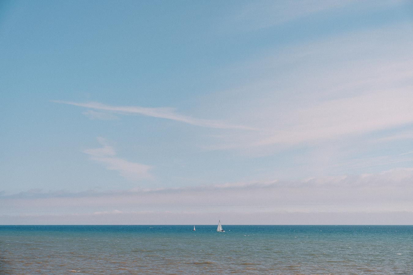Calm ocean view with two sailboats on the horizon under a clear blue sky.