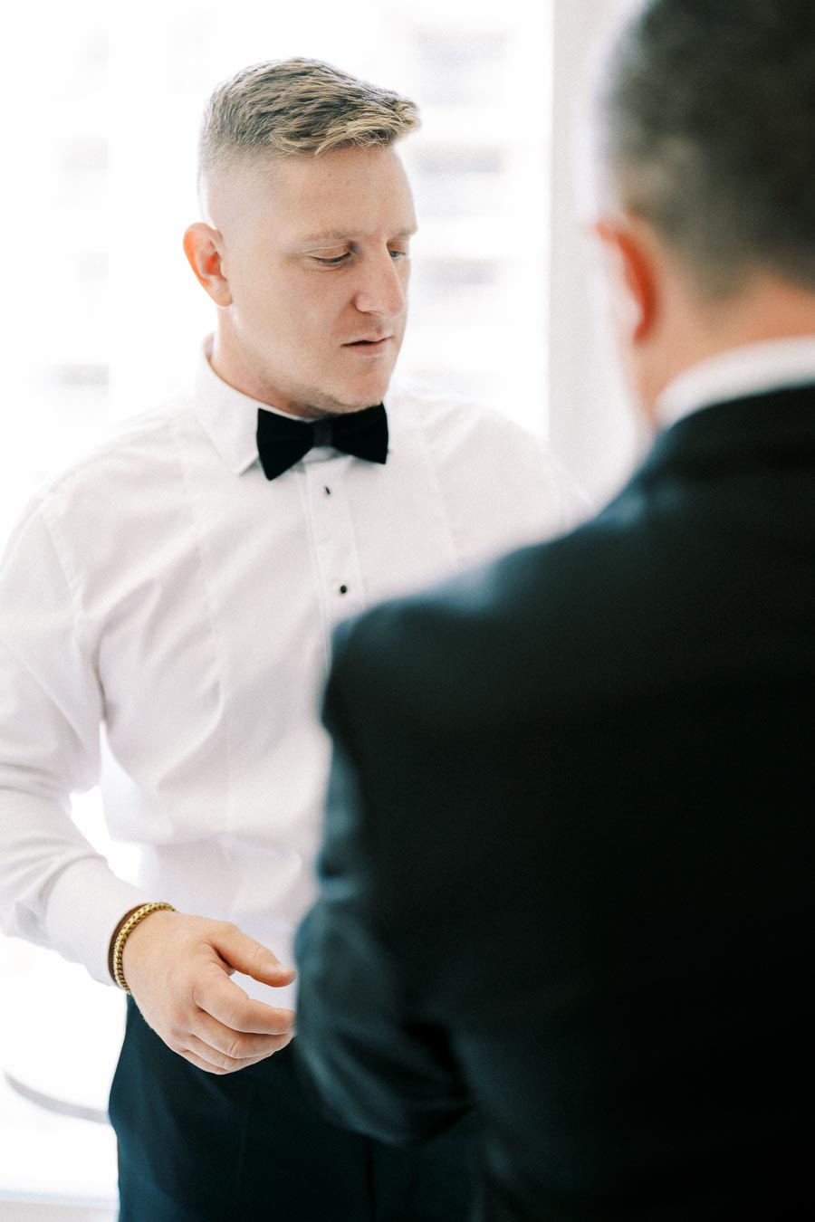 Young man in a white dress shirt and black bow tie at a formal event, standing next to another person.