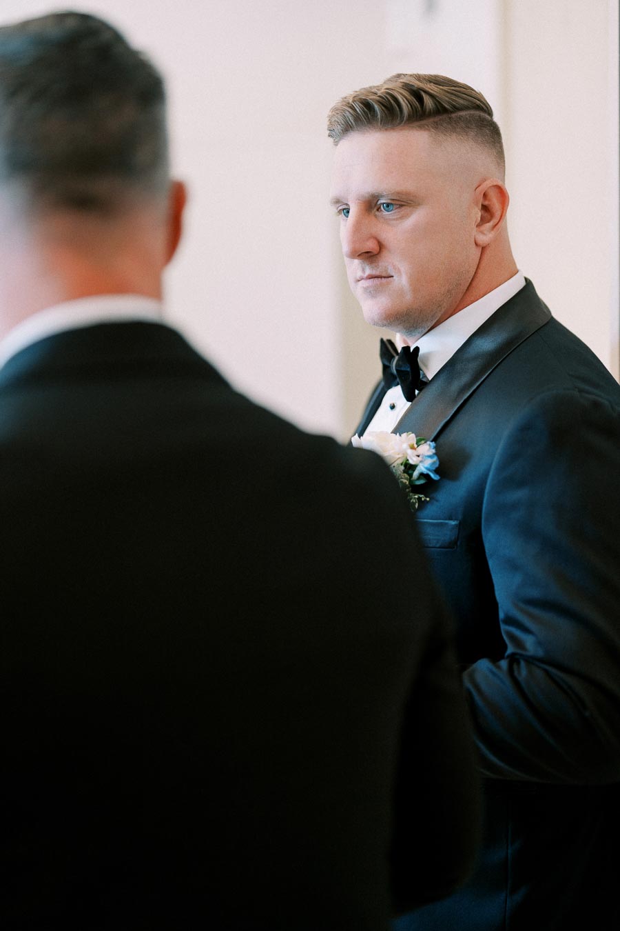 Man in formal black suit with boutonniere, looking attentively, preparing for a formal event or wedding.