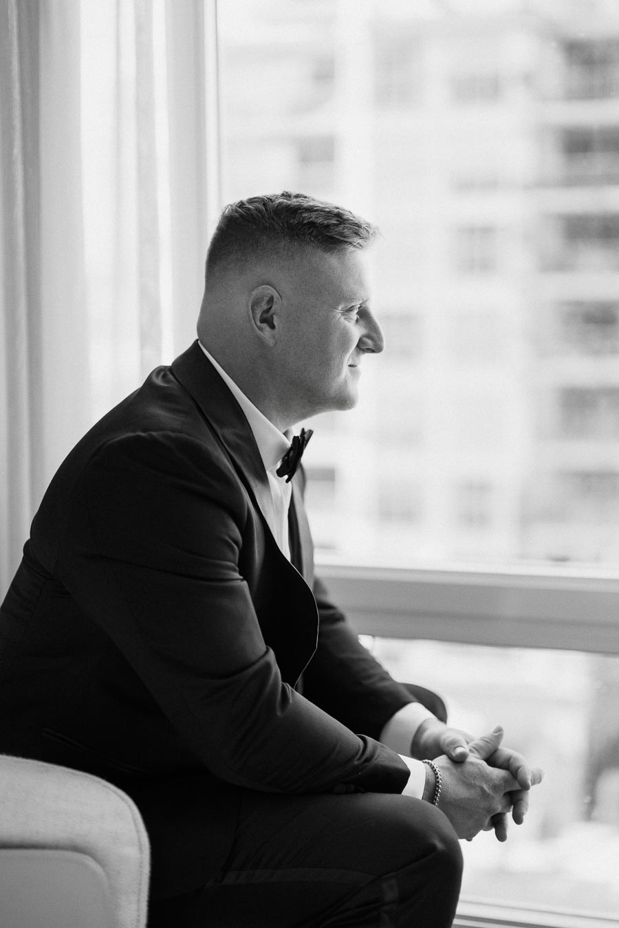 Black and white image of a man in a suit sitting thoughtfully by a window, looking outside.