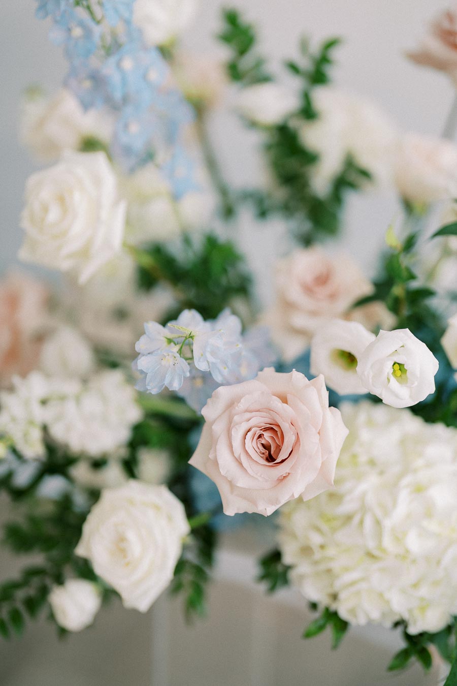 Delicate pastel bouquet featuring soft pink roses, white blooms, and light blue flowers, arranged with lush green foliage for an elegant floral display.
