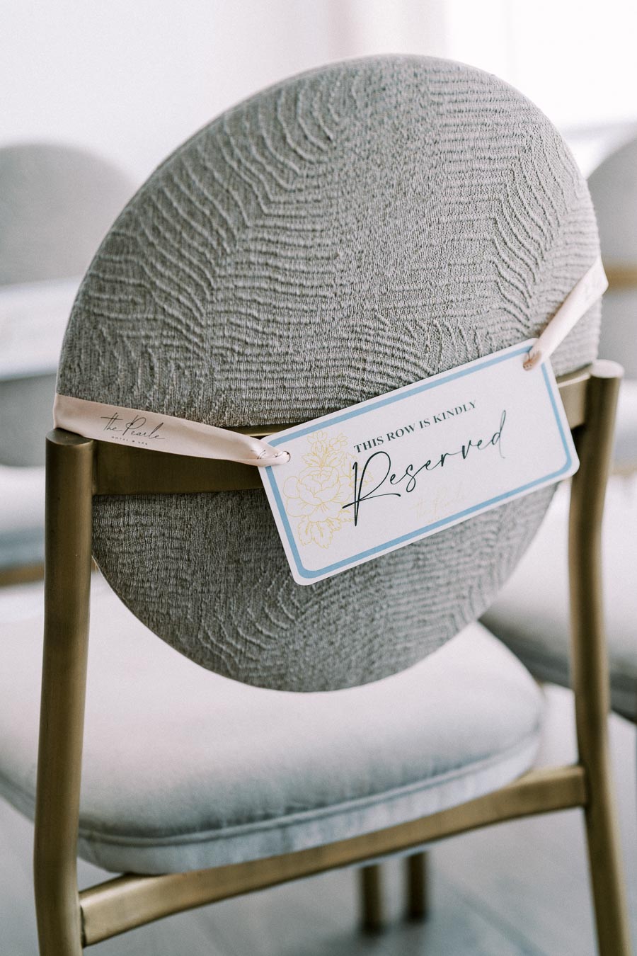 Elegant wedding ceremony chair with a textured gray backrest and a Reserved sign attached, indicating a private setting.