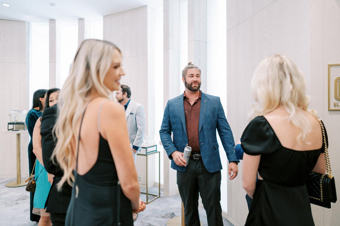 Group of well-dressed people socializing at an elegant indoor event, featuring a modern, minimalist interior design with muted tones.