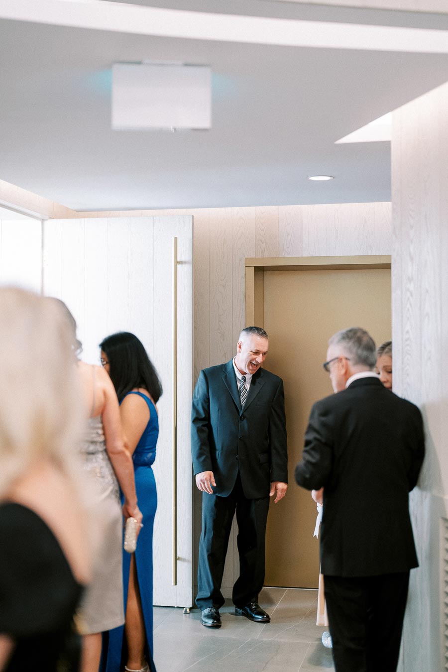 A group of people dressed in formal attire socializing near an open door in a well-lit room.