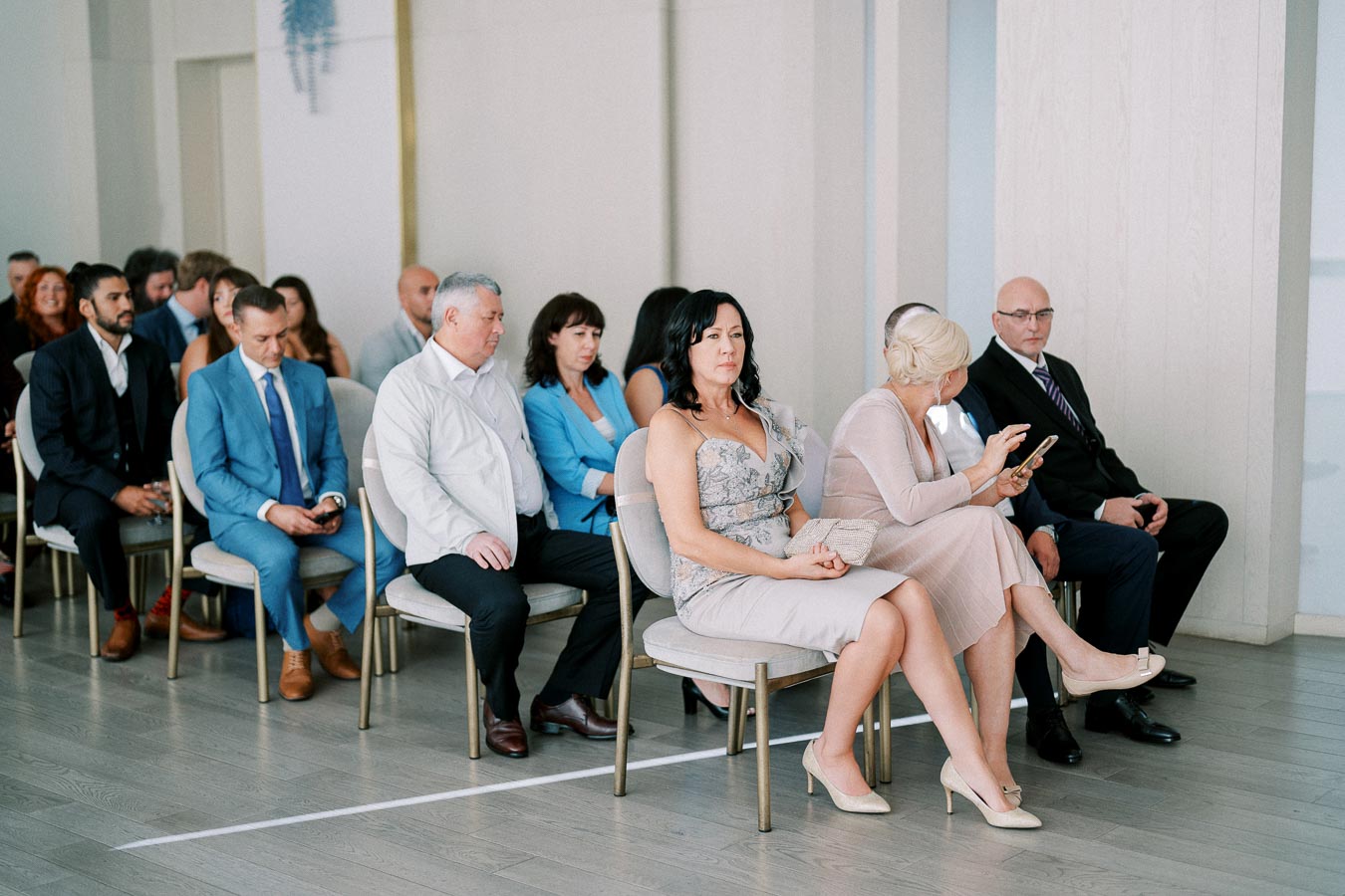 A group of people sitting in rows at an indoor event venue, dressed in formal attire.