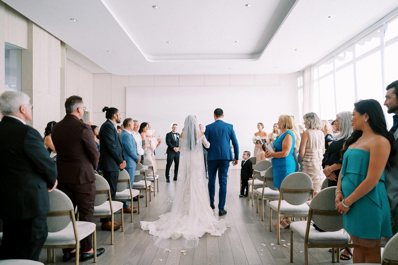 Bride and groom walking down the aisle at an indoor wedding ceremony with guests standing and watching in a bright, modern venue.