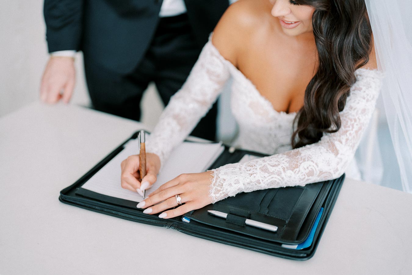 Bride signing marriage certificate in elegant lace dress during wedding ceremony.