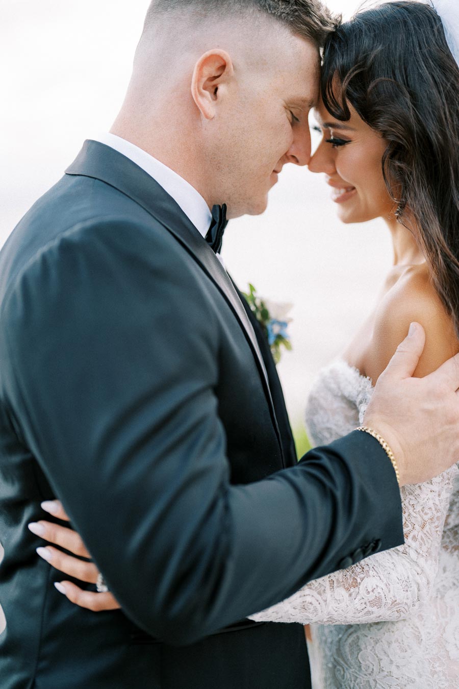 Elegant bride and groom embracing on wedding day, wearing a black tuxedo and lace gown, showcasing romantic connection and love.