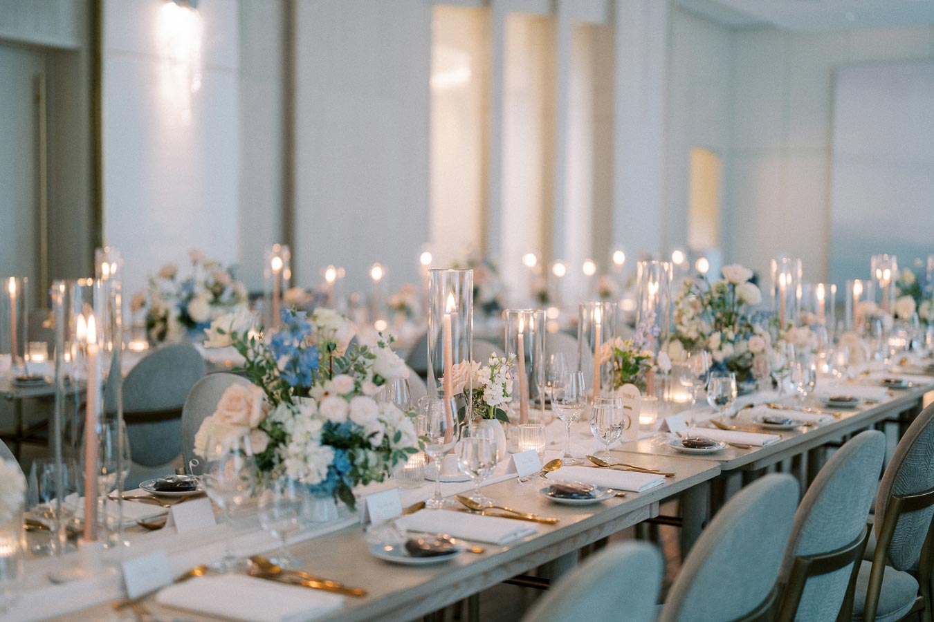 Elegant wedding reception table setting with floral arrangements, tapered candles, and fine tableware in a beautifully lit dining room.