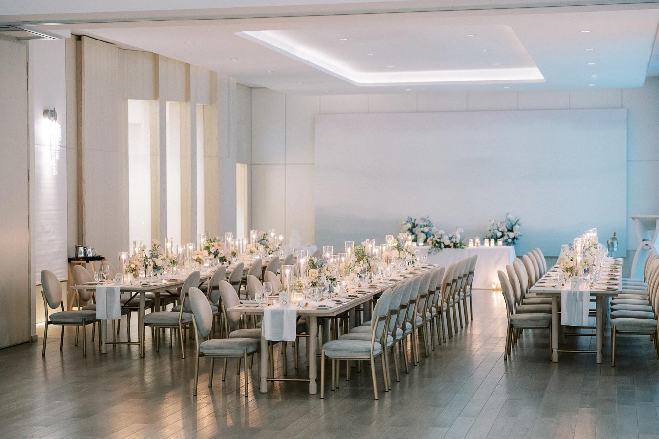 Elegant wedding reception venue with long, decorated tables, candlelit centerpieces, and floral arrangements in a modern, bright banquet hall.