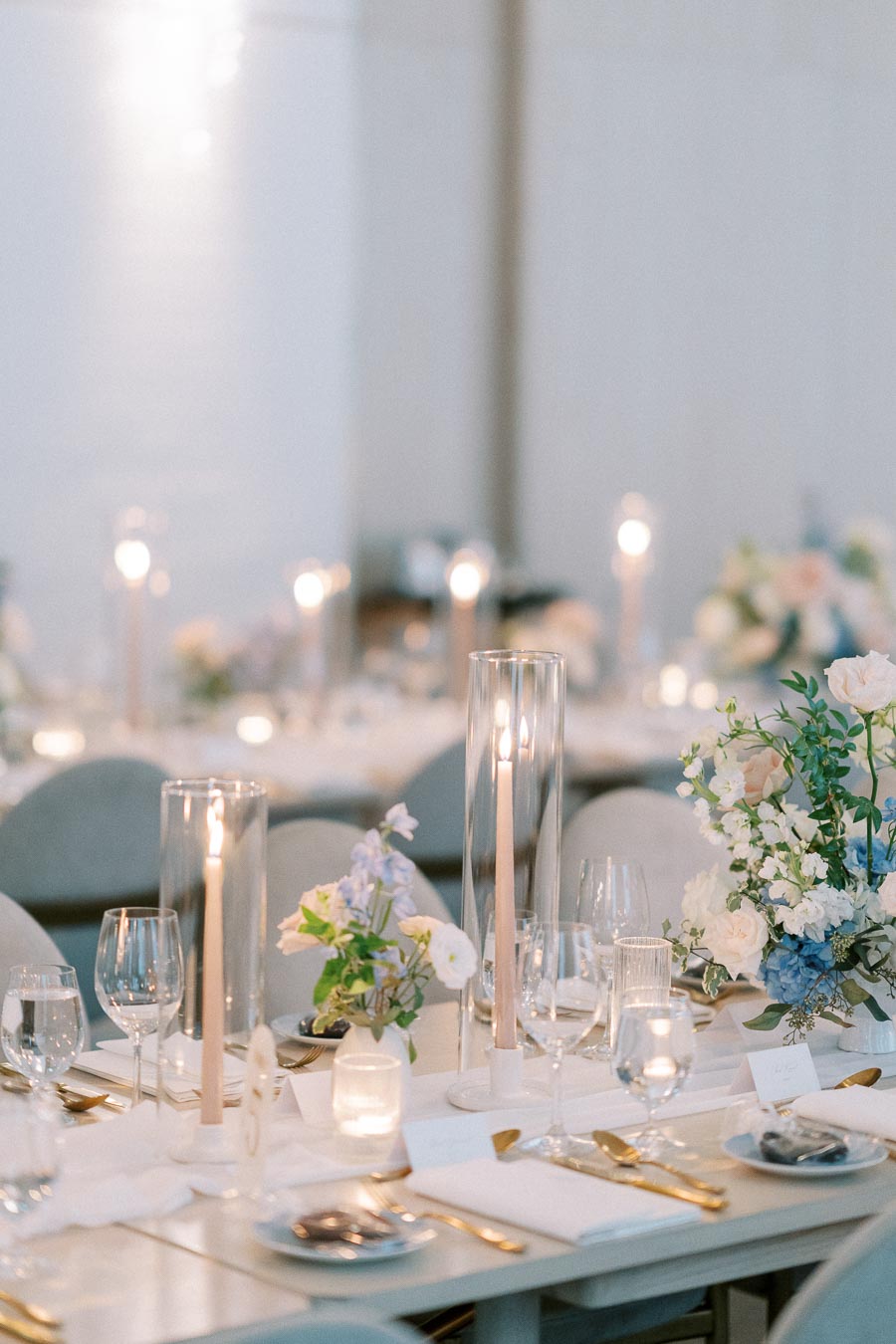 Elegant wedding table setting with tall candles, glassware, and delicate flower arrangements in pastel colors, creating a romantic ambiance.