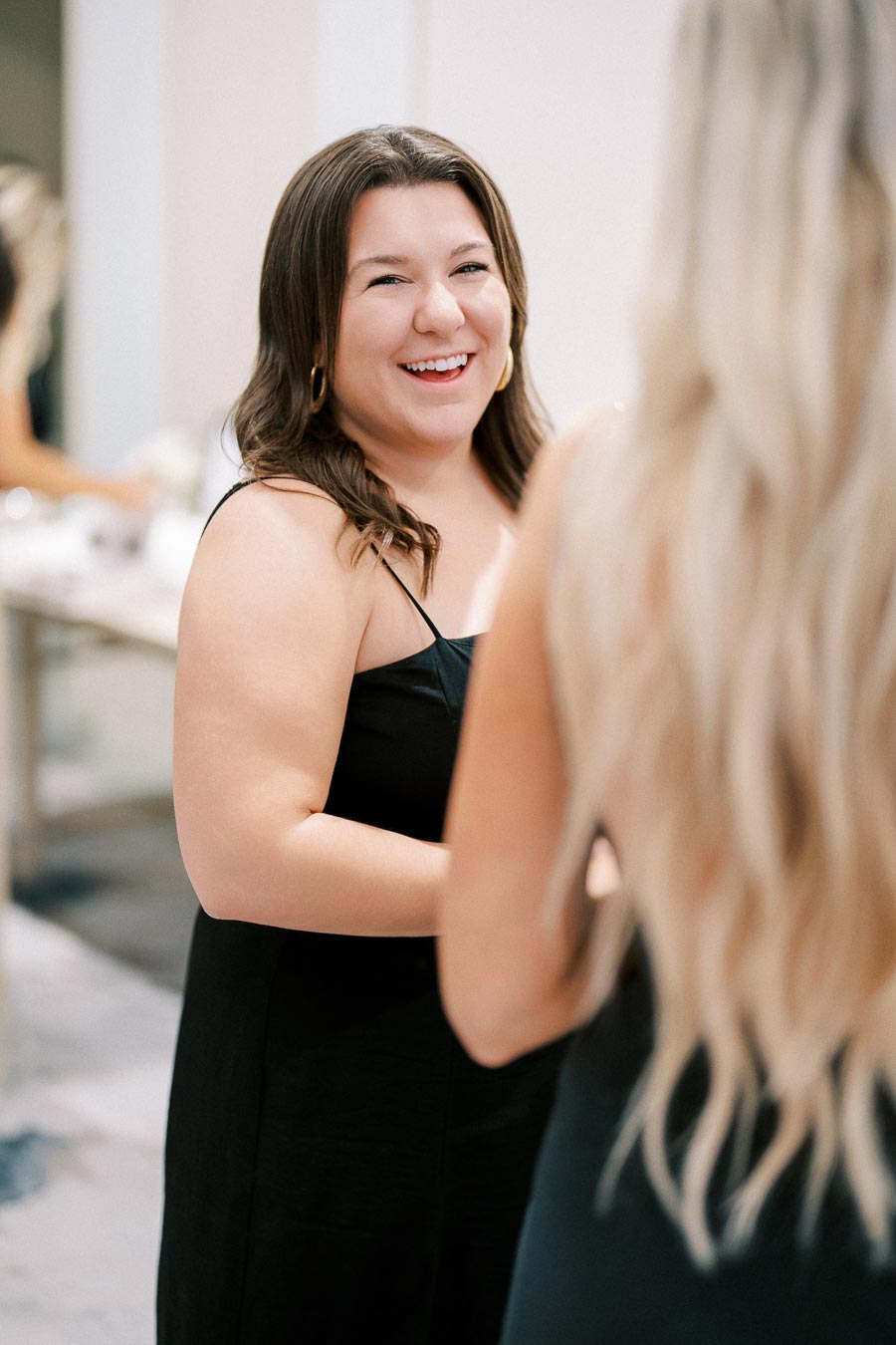 Smiling woman in a black dress engaged in conversation at a social event, highlighting joyful interaction and elegant attire.