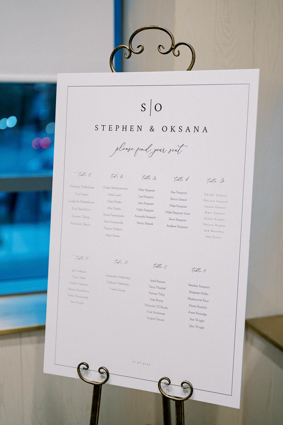 Wedding seating chart for Stephen and Oksana's celebration, featuring a list of guest names organized by table numbers, displayed on an elegant stand.