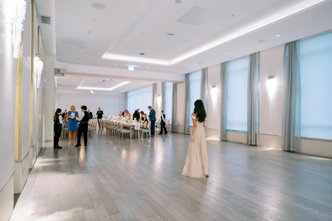 Elegant banquet hall with guests mingling and tables set for an event, featuring soft lighting and large windows in a modern venue.