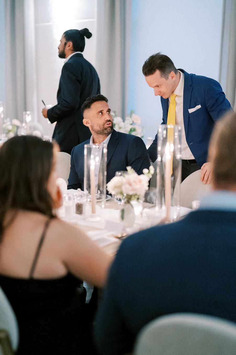 Elegant dinner event with guests in formal attire, white floral centerpieces, and candlelit ambiance.