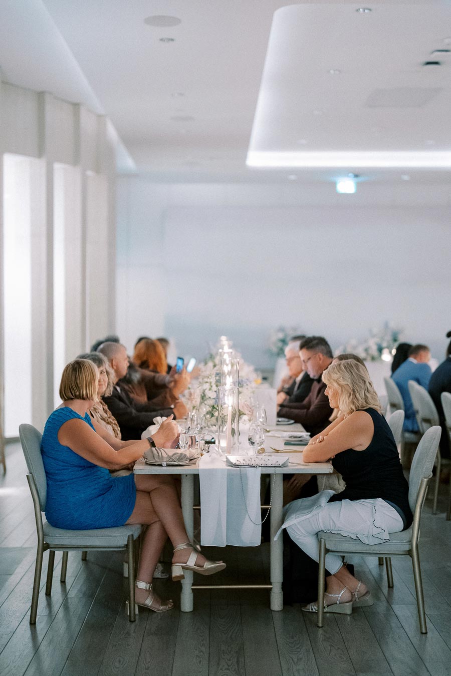 A group of people seated at a long dining table elegantly decorated with candles and floral arrangements in a modern, well-lit venue.