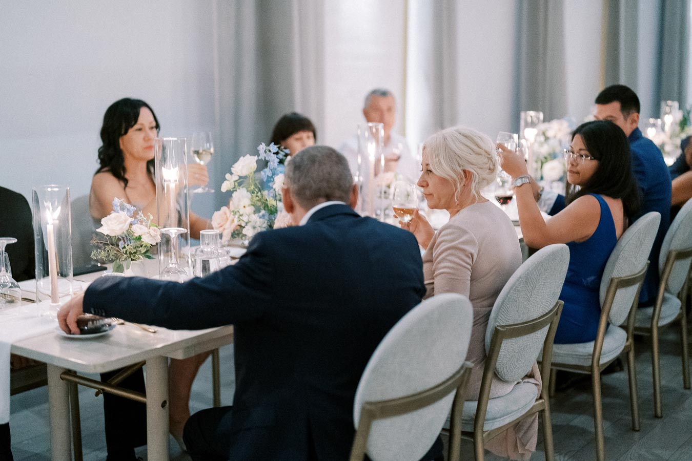 A group of people at an elegantly set dining table, enjoying a formal dinner, with glasses raised in a toast and floral centerpieces adding a decorative touch.