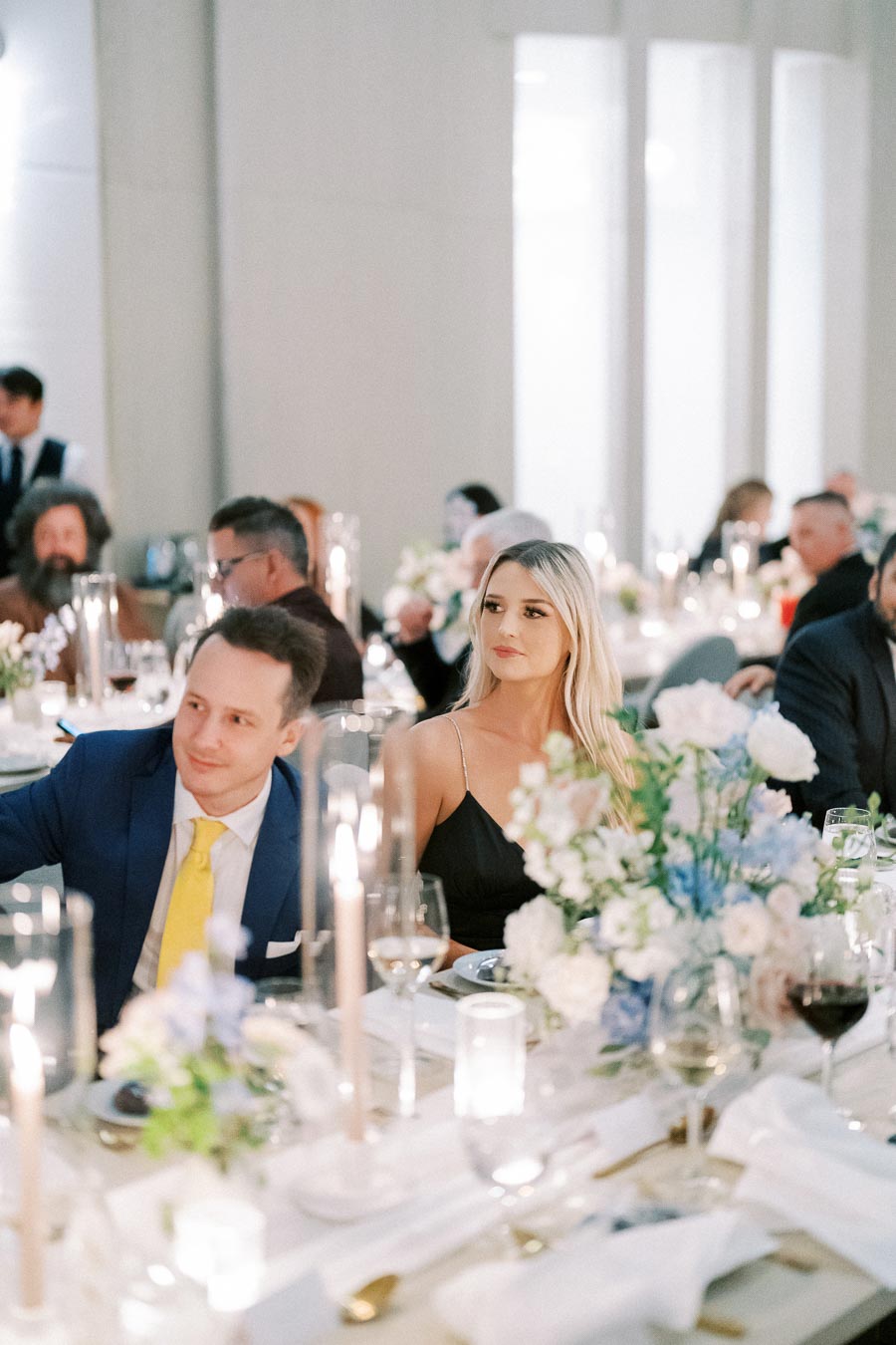 Elegant wedding reception with guests seated at a table adorned with floral centerpieces and candles, creating a sophisticated and romantic ambiance.