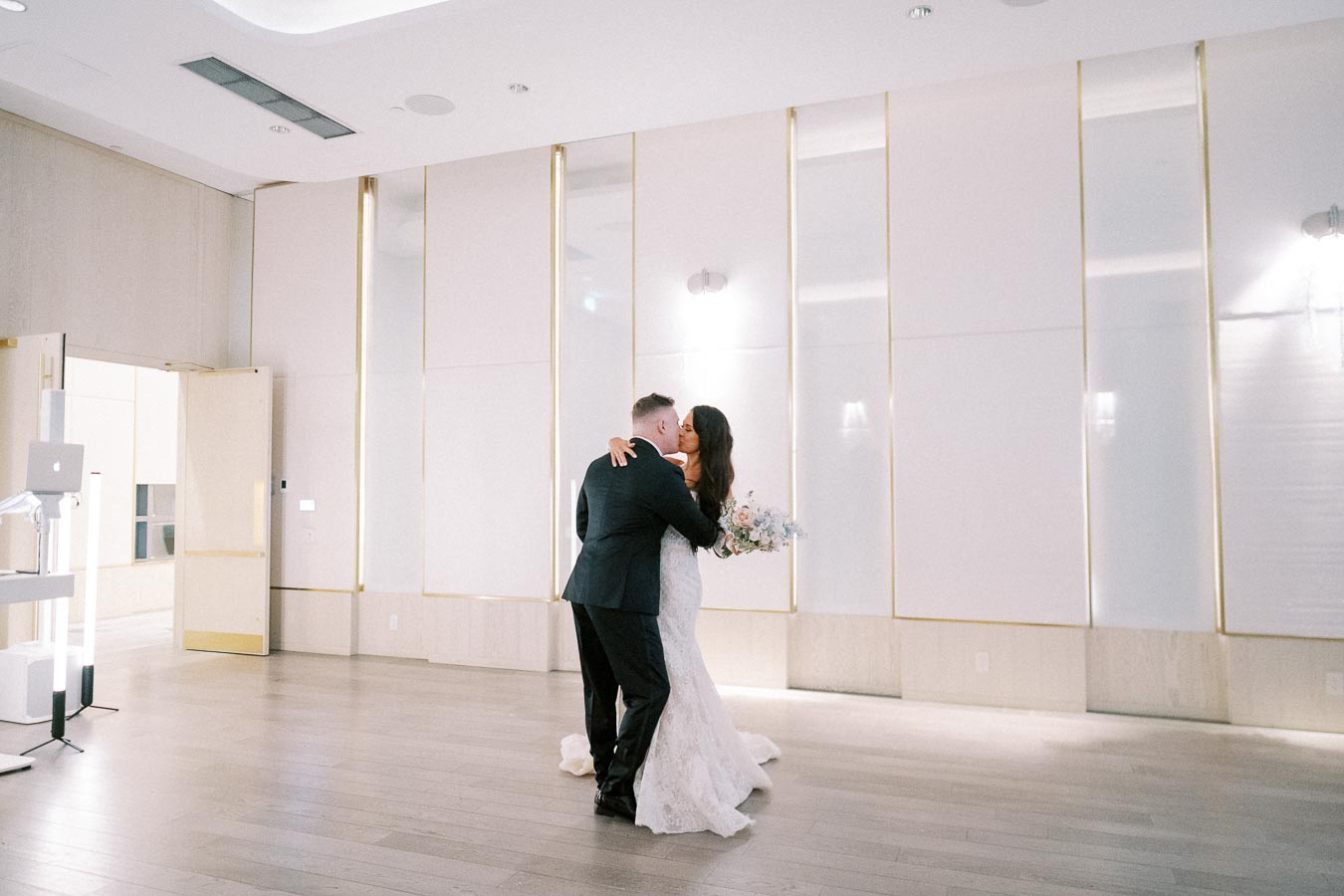 Bride and groom sharing a romantic first dance in an elegantly decorated wedding venue, highlighting a minimalist aesthetic with white and gold accents.