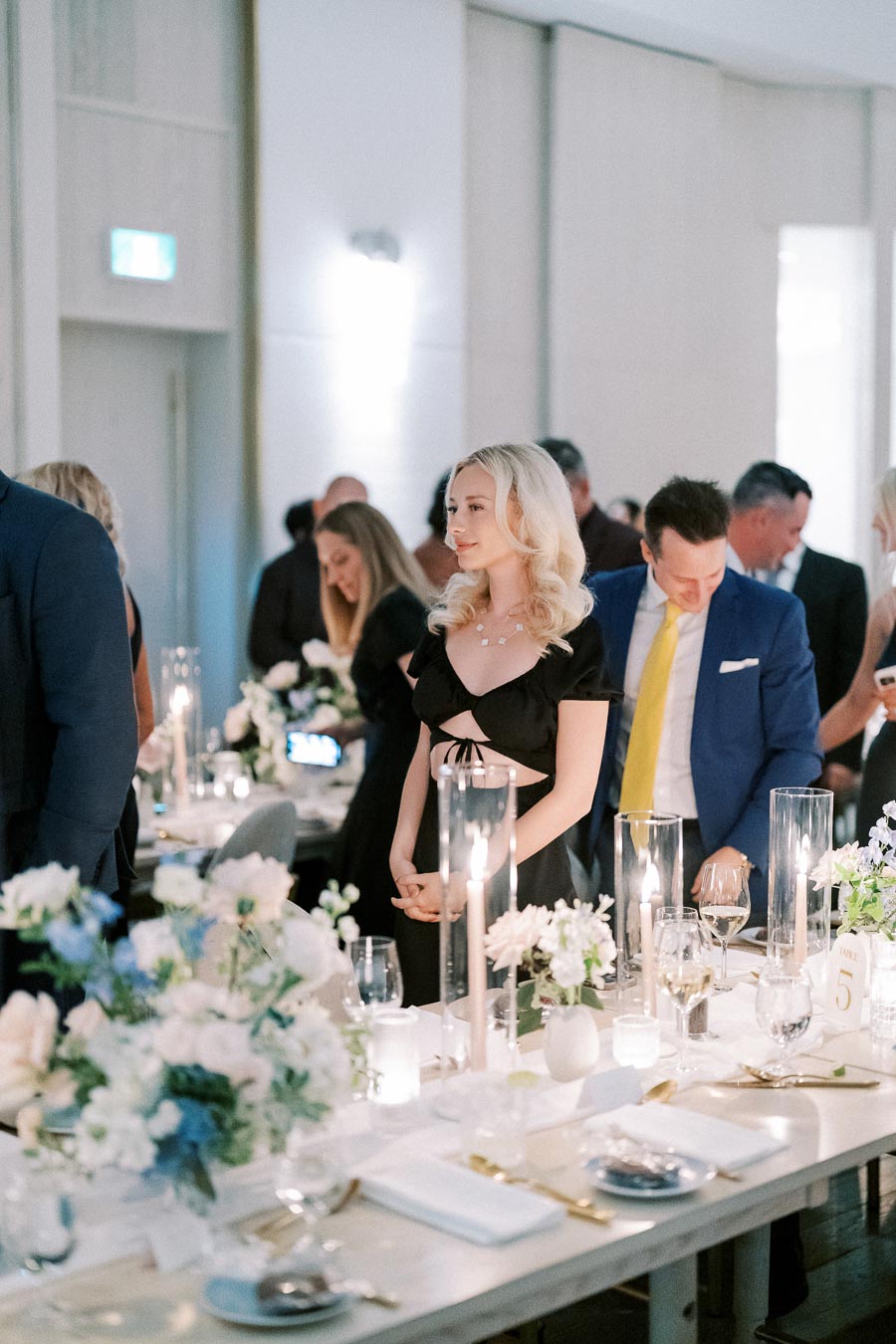 Guests elegantly dressed, gathered at a beautifully decorated wedding reception with floral arrangements and candlelit tables.