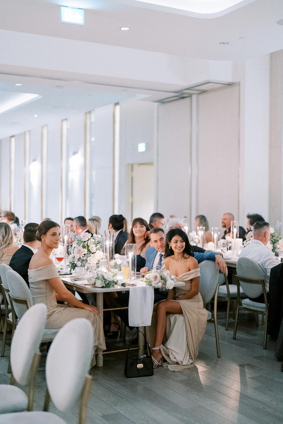 Elegant wedding reception with guests seated at beautifully decorated tables adorned with floral arrangements and candles in a sophisticated event venue.