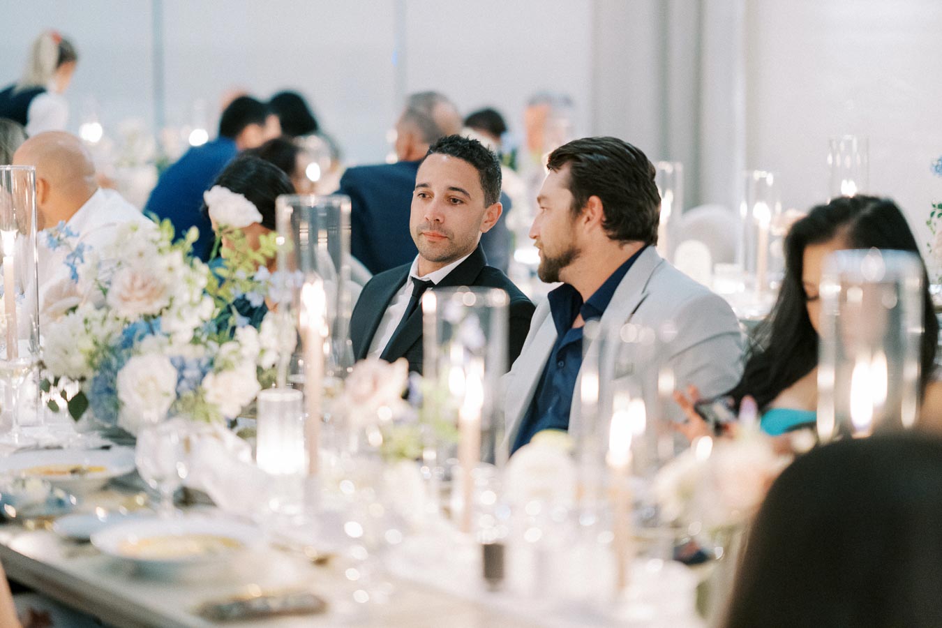 Guests seated at an elegant event, with beautifully arranged floral centerpieces and soft candle lighting creating a sophisticated atmosphere.