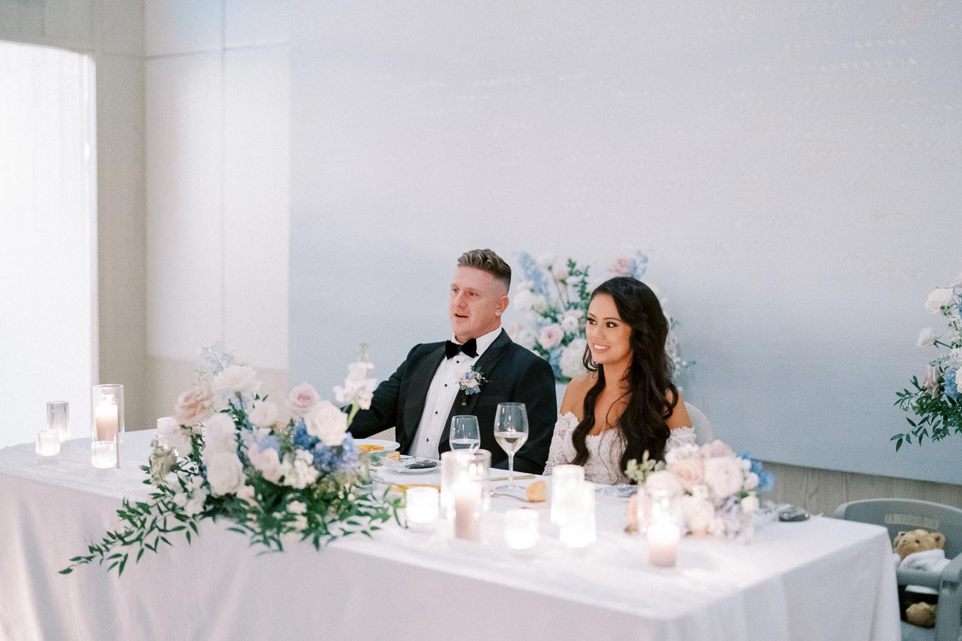 Elegant wedding couple seated at a beautifully decorated reception table with floral arrangements and candles.
