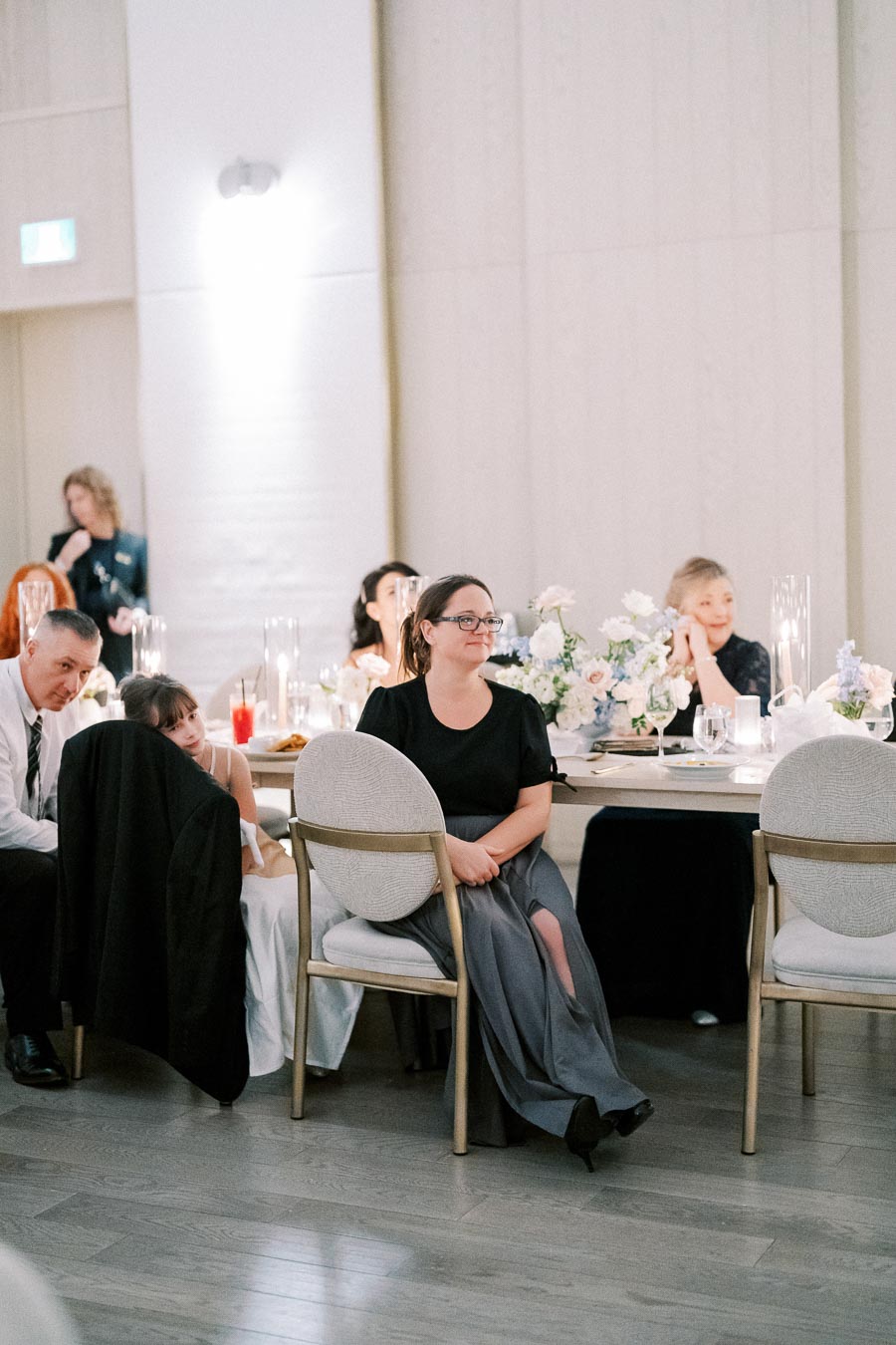 Group of wedding guests seated at a reception table, elegantly decorated with floral centerpieces and candles, enjoying the celebration in a modern venue setting.