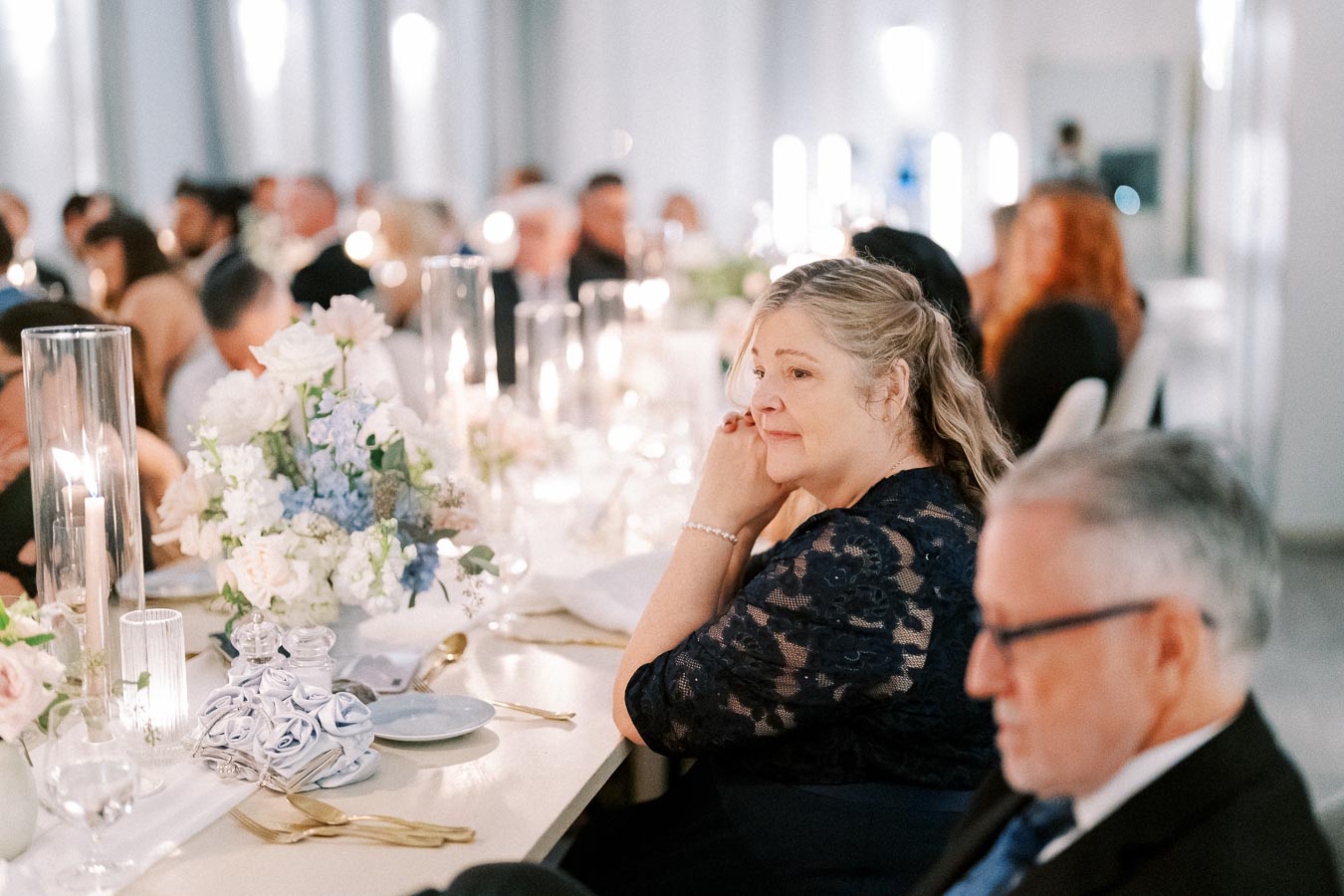 Elegant wedding reception with guests seated at a beautifully decorated table adorned with flower arrangements and candle centerpieces.