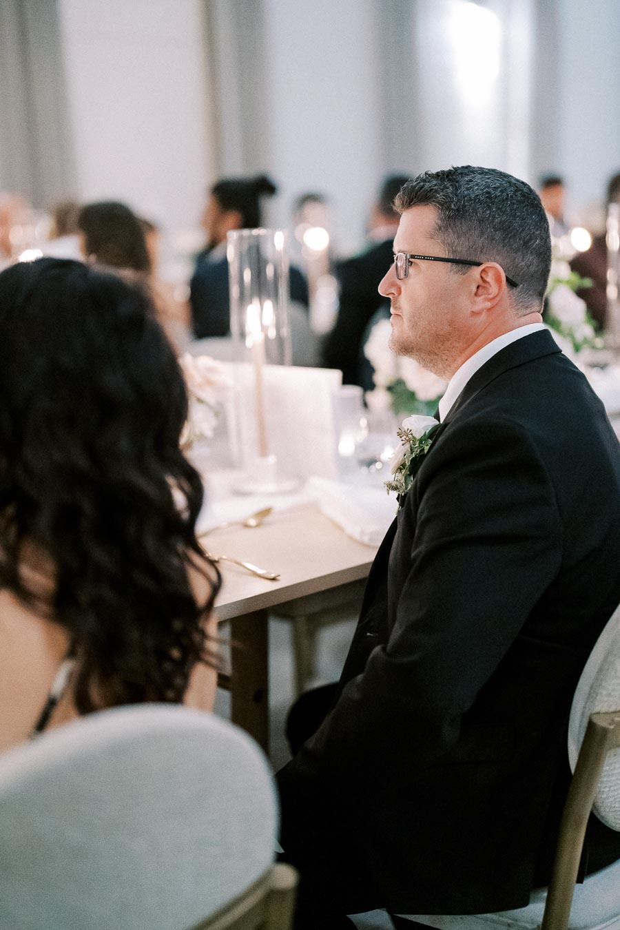 Man in formal attire attending an elegant event at a beautifully decorated table with candlelight ambiance.