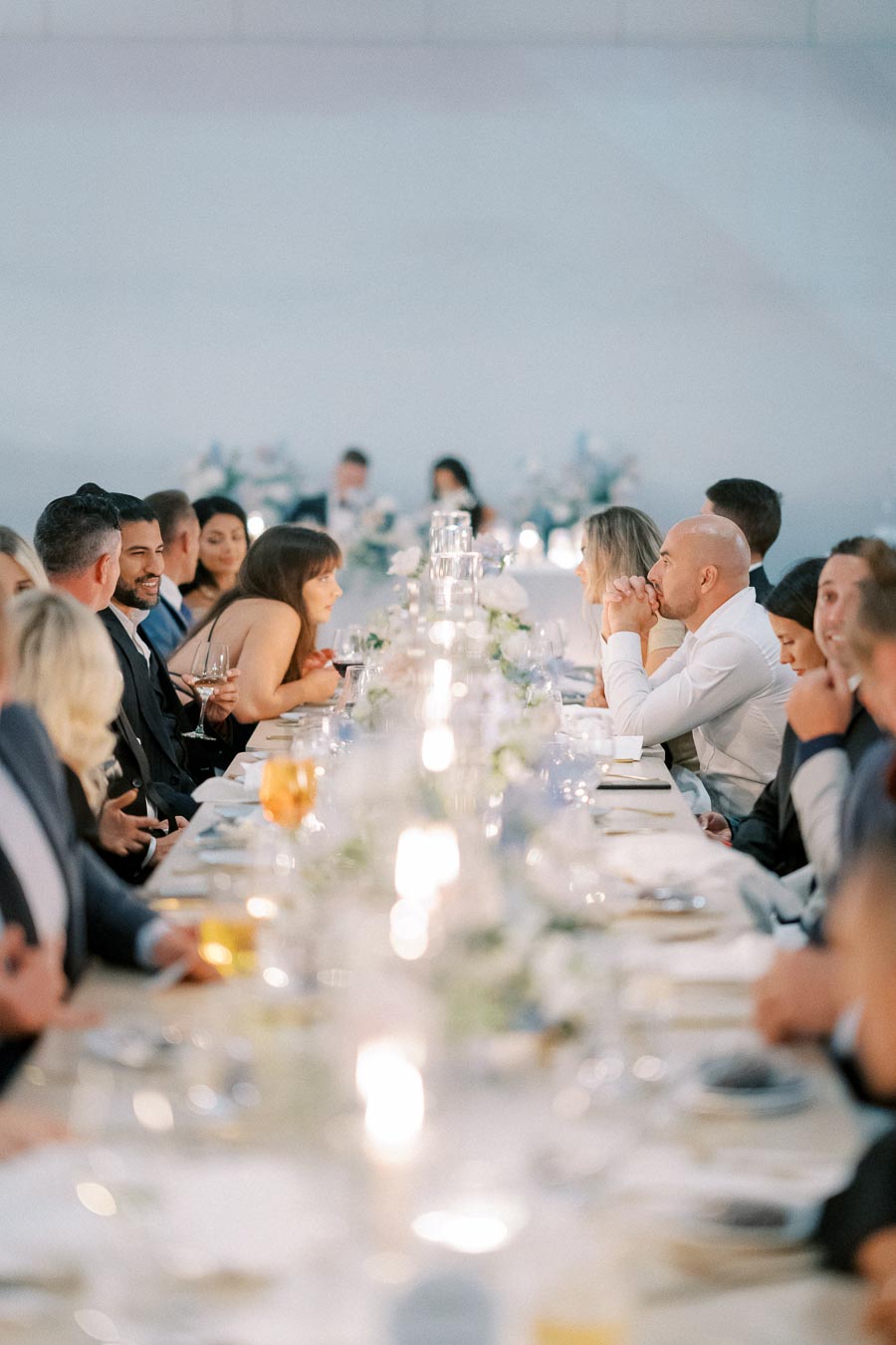 Elegant dinner party with guests seated at a long, candle-lit table adorned with white floral arrangements, creating a sophisticated ambiance.