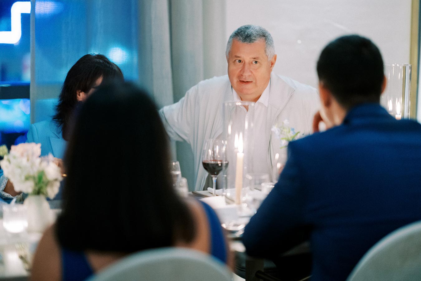 A group of people enjoying an elegant dinner with lit candles and wine glasses, focusing on a man speaking.