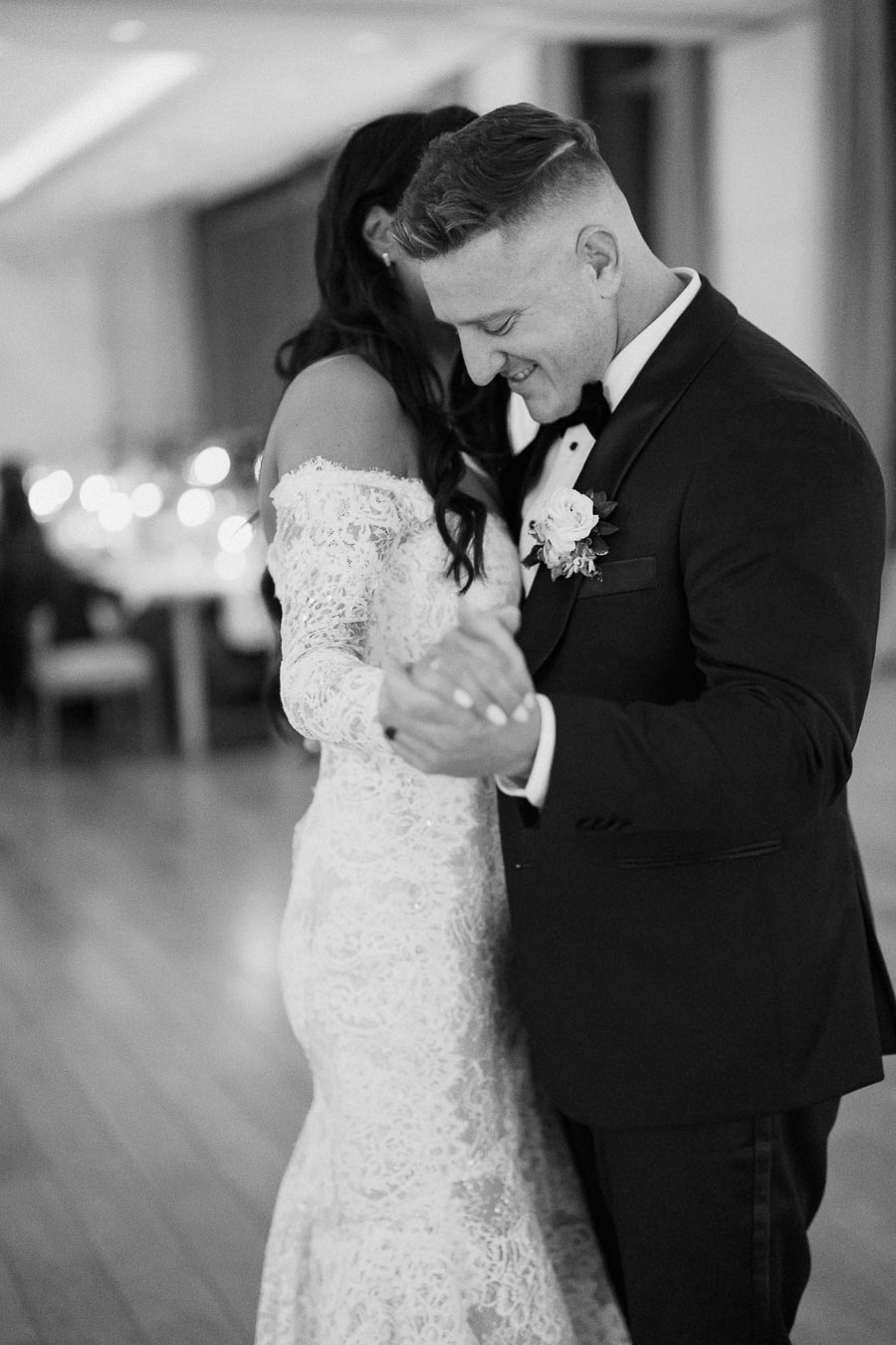 Couple sharing a romantic dance at a wedding, with the groom in a classic tuxedo and the bride in an elegant lace gown, capturing a tender moment on the dance floor.