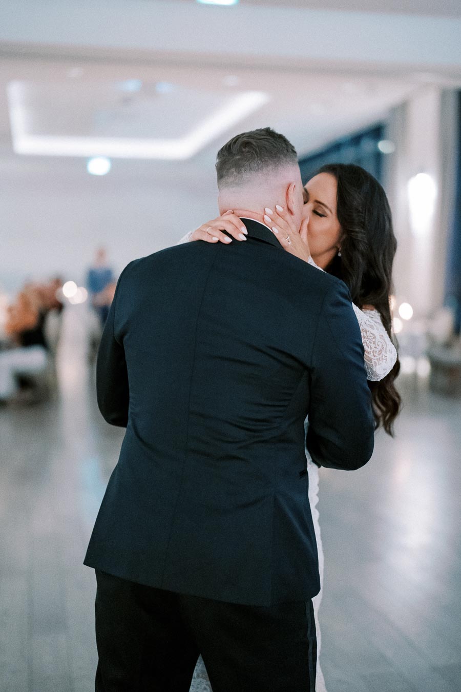 Romantic wedding couple embracing and kissing on the dance floor in elegant attire, capturing a memorable moment in a beautifully lit reception venue.
