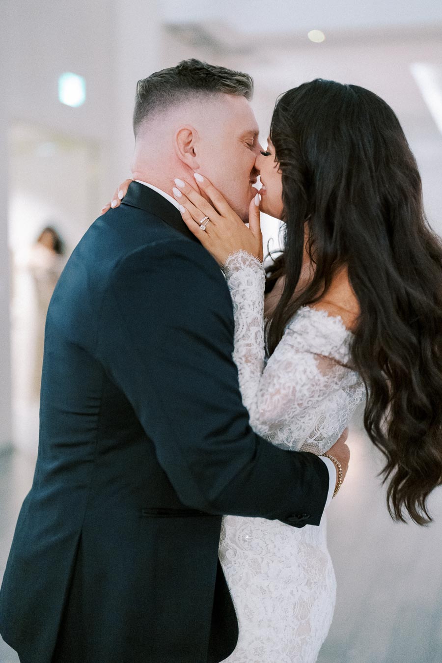 Bride and groom sharing a romantic kiss in wedding attire, showcasing a beautiful lace wedding dress and a classic suit, capturing a tender moment of love on their special day.