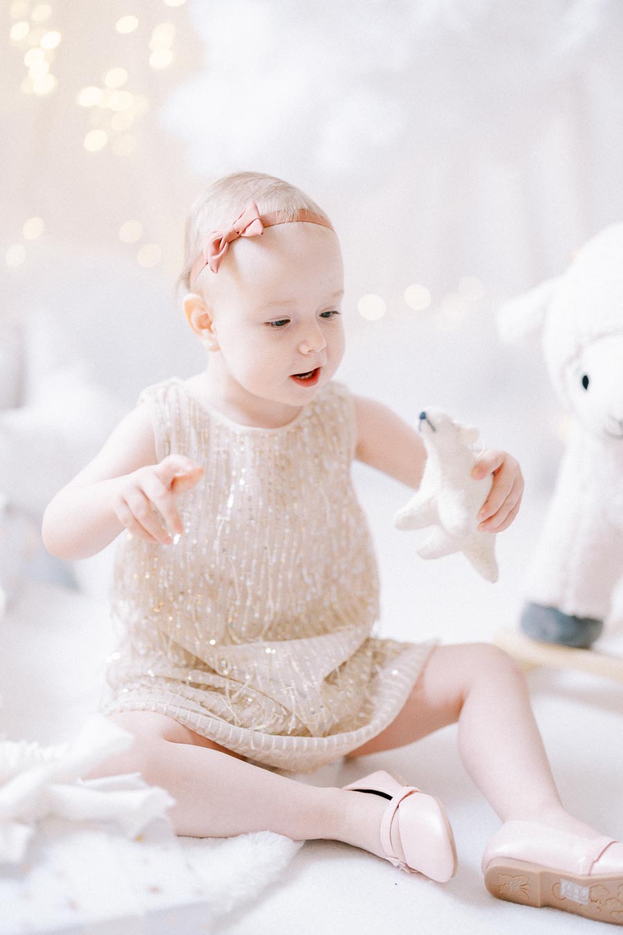A young child in a sparkly dress plays with a soft toy polar bear against a festive, dreamy background with warm lights and soft textures.
