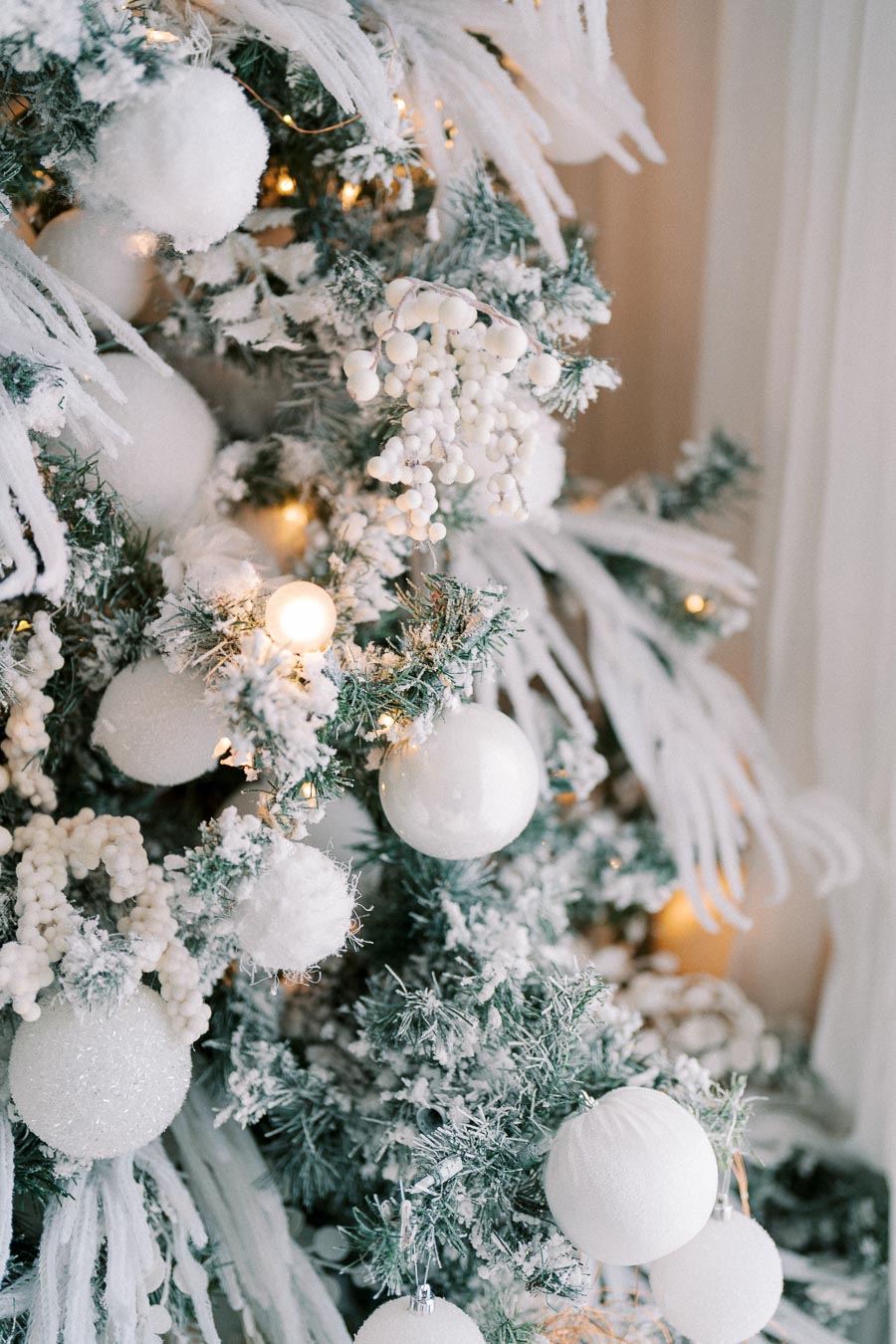 Festive Christmas tree adorned with white ornaments and snow-covered branches, elegantly decorated with lights and berries, creating a winter wonderland theme.