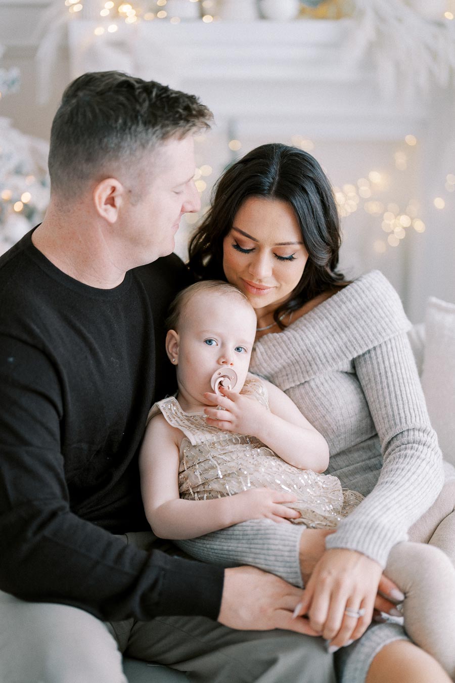 A cozy family moment with a man, woman, and baby in light festive surroundings, capturing warmth and togetherness.