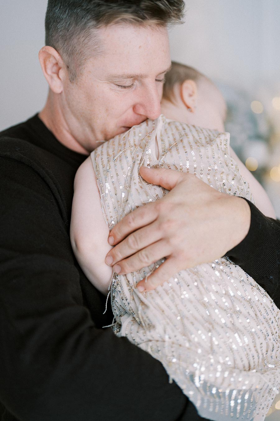 A gentle, loving father holding his baby dressed in a sparkly outfit, embodying warmth, care, and tenderness.