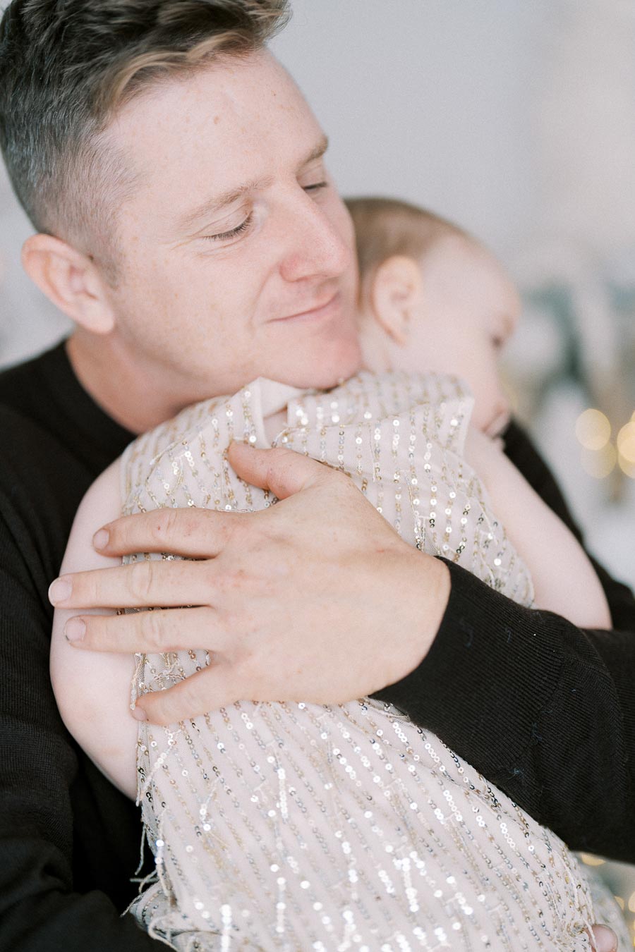 A loving father embraces his baby daughter, both dressed elegantly. The baby is wearing a shimmering sequined dress, symbolizing a joyful family moment.