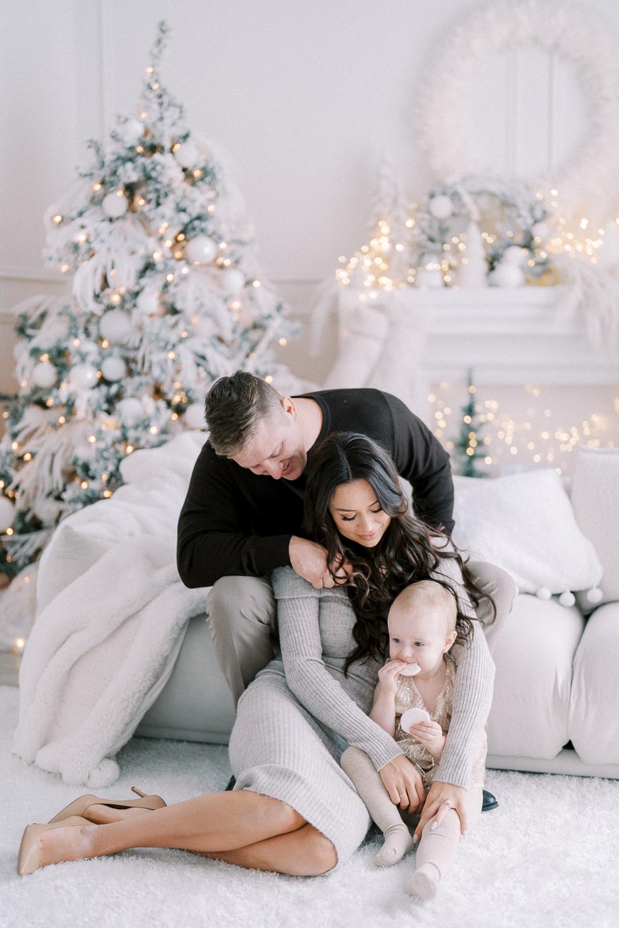 Cozy family scene with parents and baby enjoying a festive holiday setting, featuring a beautifully decorated Christmas tree and warm, soft lighting in a living room.