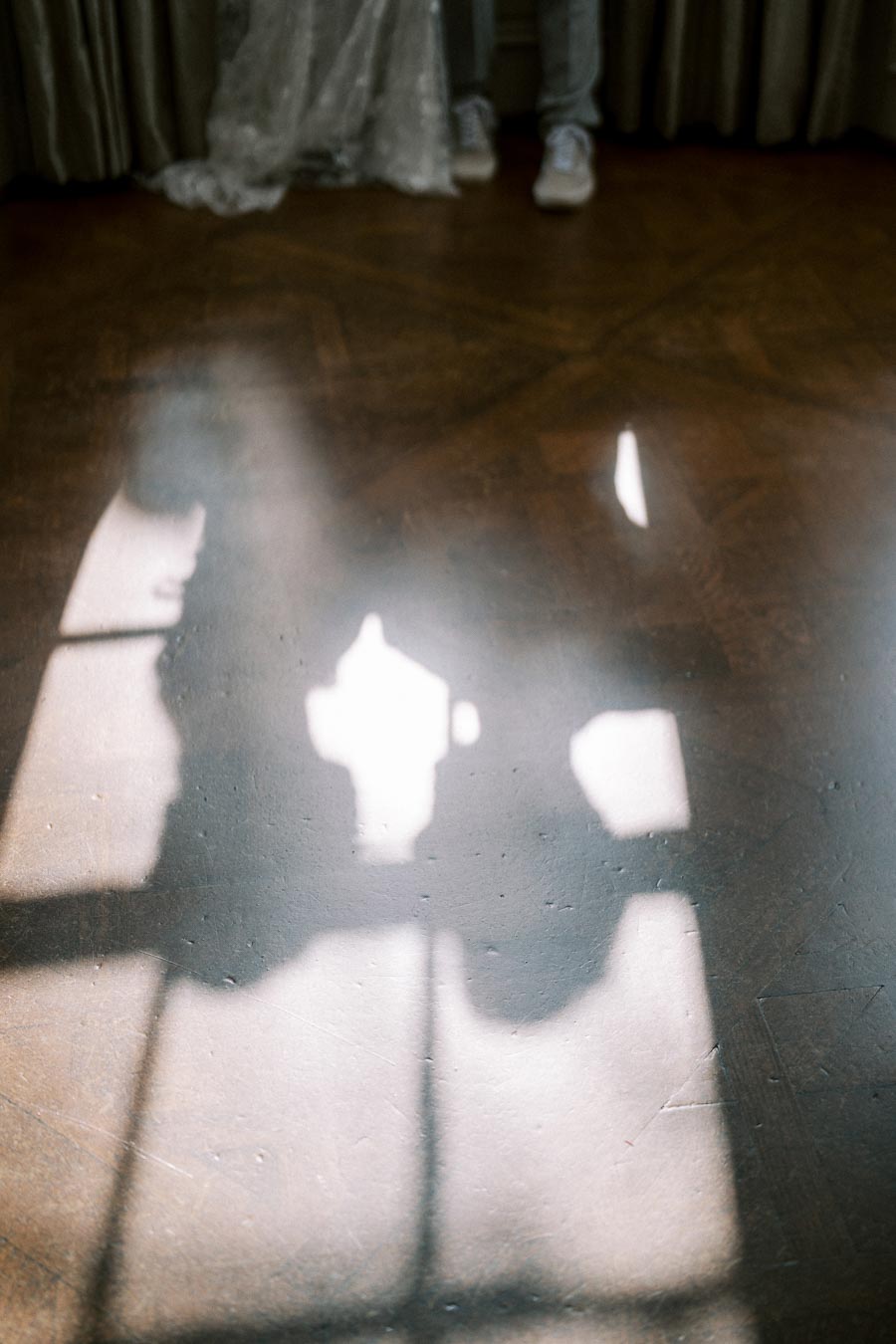 Shadow of a bride and groom holding hands on a wooden floor, with sunlight streaming through a window, creating a romantic and intimate atmosphere.